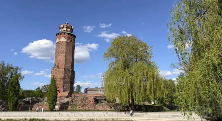 Wieża zamkowa w Brodnicy, otoczona zielenią, na tle błękitnego nieba z chmurami. Piękny dzień na Pojezierzu Brodnickim.