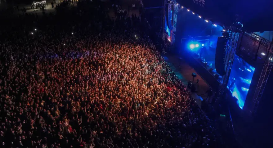 Tłum ludzi na koncercie, rozświetlony sceną i światłami. Atmosfera przed festiwalem Before Festival jest elektryzująca.