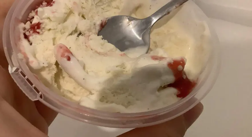 Ein Löffel steckt in einem Becher mit schmelzendem, altem Eis mit Erdbeersauce.