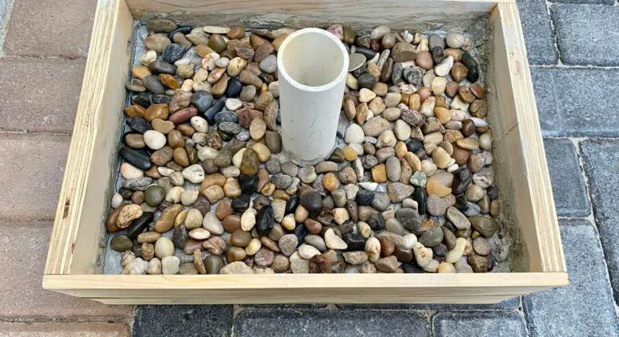Base per ombrellone fai da te: un contenitore in legno riempito di ghiaia con un tubo centrale per l'asta.