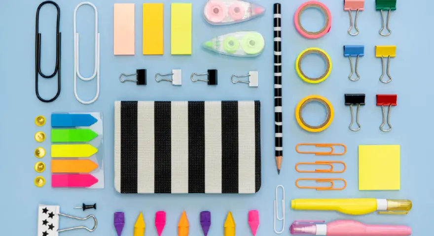 Un surtido vibrante de material de oficina lista para usar: clips, notas adhesivas, cintas, lápices y más, organizados sobre un fondo azul claro.