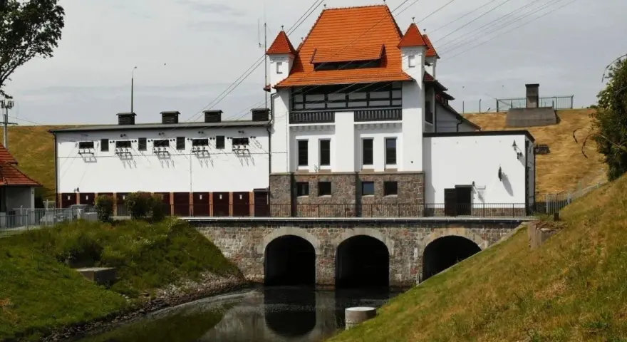 Elektrownia wodna Straszyn z charakterystycznym czerwonym dachem i kamiennymi arkadami nad kanałem.