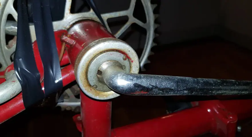 När man ska byta vevlager på cykeln syns en del av vevarmen och kedjekransen. Svart tejp håller ihop delar.