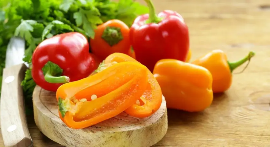 Peperoni piccoli colorati, pronti per gustose ricette. Un coltello e prezzemolo completano la scena.