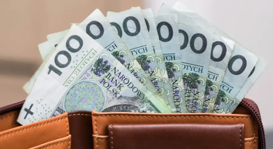 Portfel z banknotami 100 zł. Czy urlop wychowawczy jest płatny? To pytanie nurtuje wielu rodziców, a pieniądze w portfelu mogą pomóc w podjęciu decyzji.
