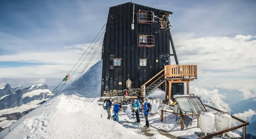 Die Capanna Margherita, eine Berghütte auf einem schneebedeckten Gipfel, mit Bergsteigern, die sich auf den Aufstieg vorbereiten.