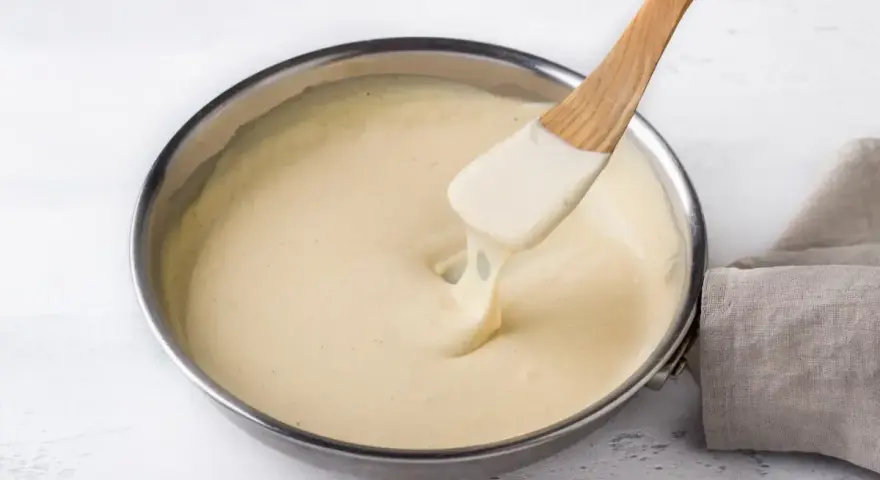 Una spatola di legno mescola una cremosa fonduta di parmigiano in una padella.