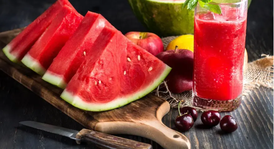 Saftige Wassermelone-Scheiben und ein Glas erfrischender Wassermelonensaft, reich an Vitaminen. Äpfel und Kirschen ergänzen das gesunde Arrangement.