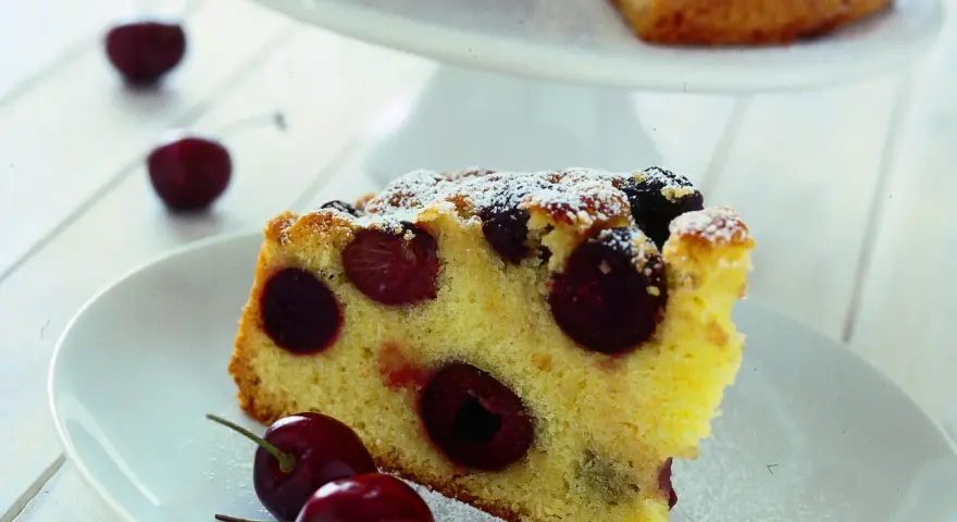 Una fetta di torta soffice e dorata, ricca di ciliegie succose, cosparsa di zucchero a velo. Perfetta per un momento di dolcezza.