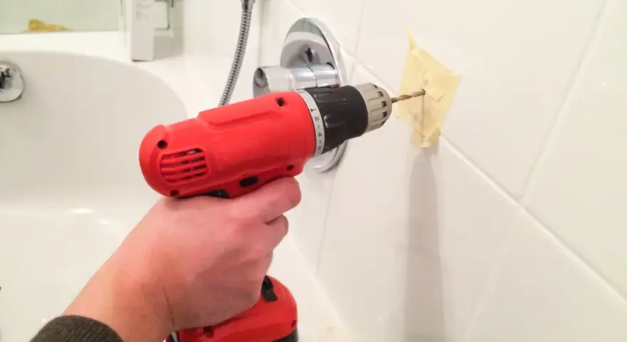 Bohren von Fliesen im Badezimmer mit einem roten Akkuschrauber. Ein Stück Klebeband schützt die Wand.