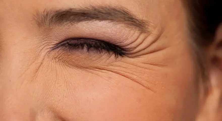 Primer plano de un ojo cerrado con maquillaje, mostrando las arrugas debajo de los ojos que marcan la expresión.