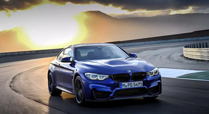 Niebieskie BMW M2 CS pędzi po torze wyścigowym podczas zachodu słońca.