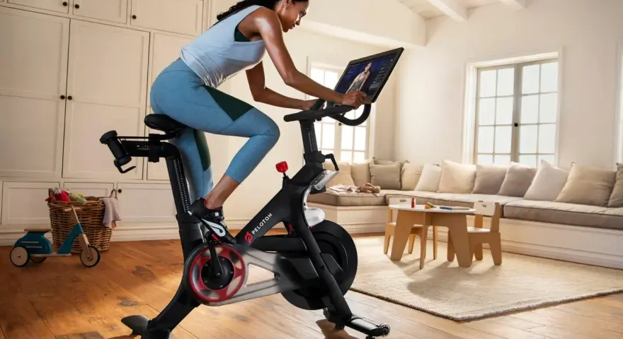 A woman rides a Peloton bike, a popular tool for peloton weight loss, in a bright, homey living room.