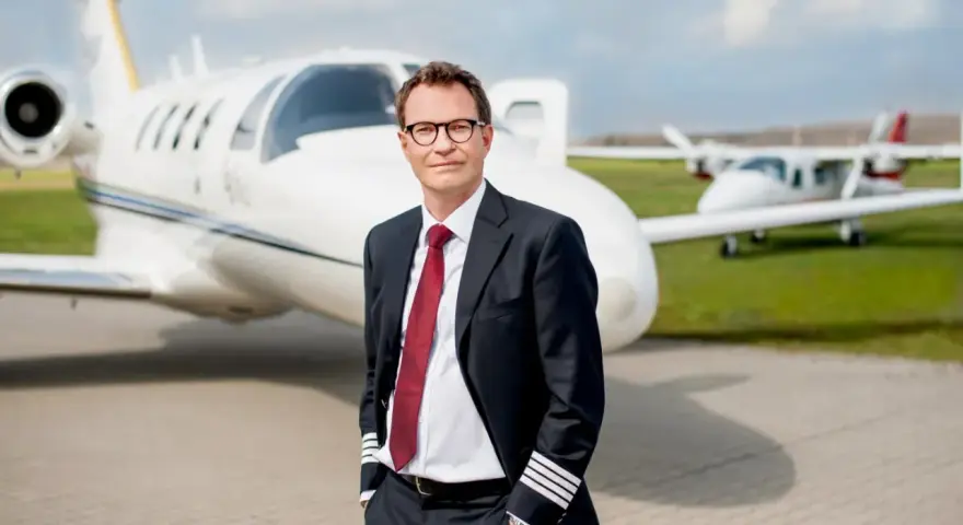 Pilot w garniturze z odznaką na rękawie, stojący przed odrzutowcem. Zastanawiasz się, ile zarabia pilot Ryanair?