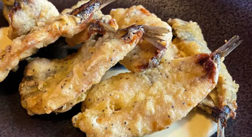 Crujientes boquerones fritos, dorados y servidos sobre una cremosa salsa.