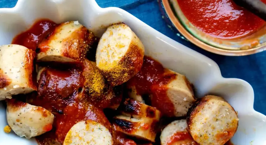 Leckere Currywurst mit einer würzigen Currywurst-Sauce und Currypulver bestreut, serviert in einer weißen Schale.