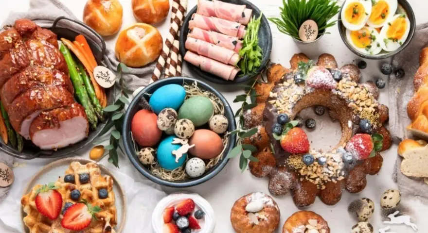 A festive Easter feast in Europe, featuring a glazed ham, colorful eggs, sweet breads, and a decorated cake.