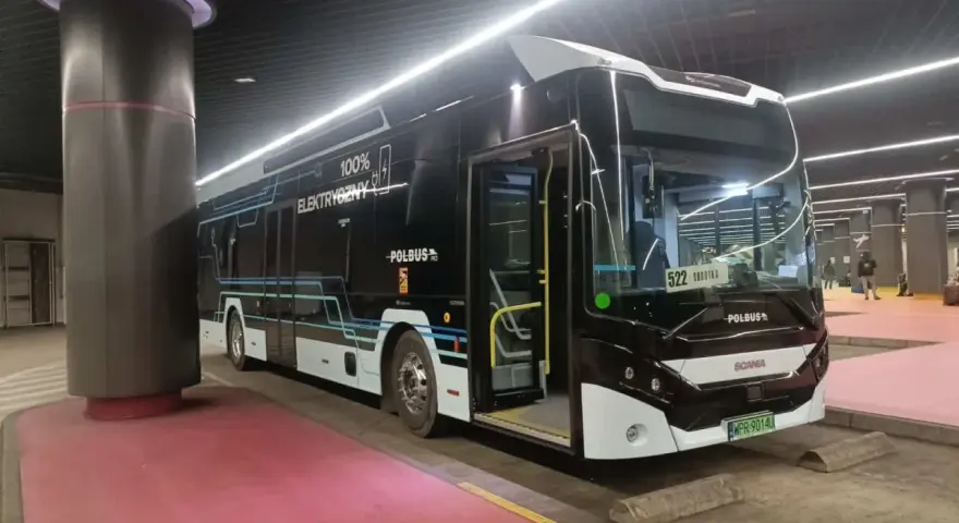 Nowoczesny, czarny autobus elektryczny z napisem "100% ELEKTRYCZNY" stoi na przystanku.