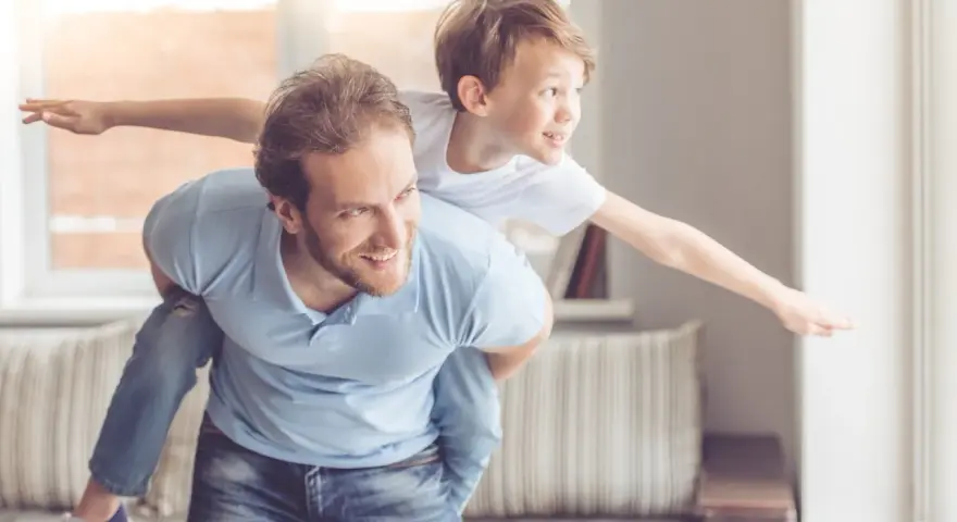 Ein Vater trägt seinen Sohn auf dem Rücken. Der Sohn streckt die Arme aus wie ein Flugzeug. Das sind meine worte an meinen sohn: Flieg hoch!