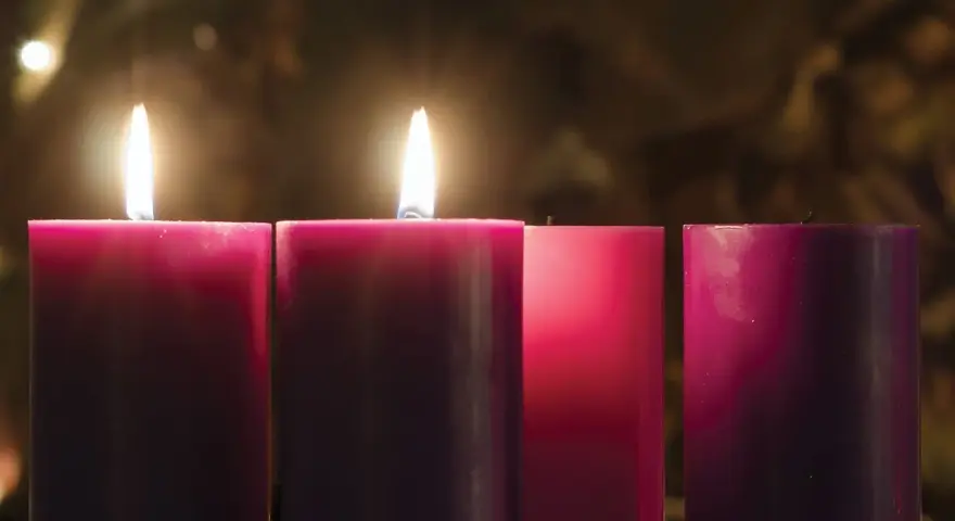 Two lit candles glow on the 2nd Sunday of Advent, their flames casting a warm light on the surrounding purple and pink candles.