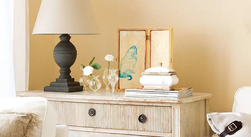 Cómoda de estilo vintage con cajones pintados a la tiza, decorada con lámpara, jarrones con flores y un cuadro de gato.