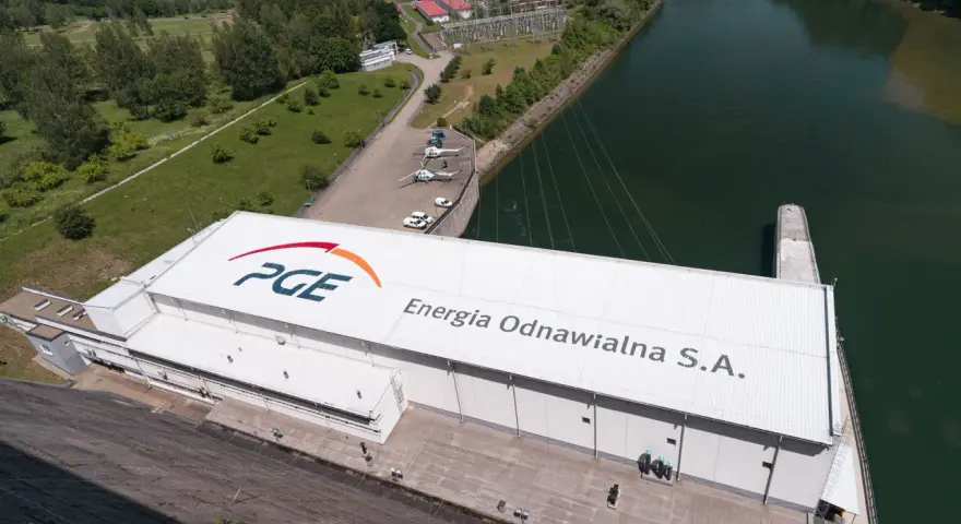 Widok z lotu ptaka na elektrownię wodną PGE Energia Odnawialna S.A. z charakterystycznym logo. Widać tam też helikoptery i samochody.