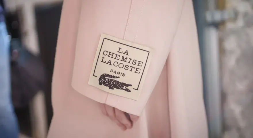 Różowy płaszcz z metką "LA CHEMISE LACOSTE PARIS" z krokodylem, symbol luksusowych marek ubrań.