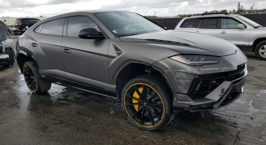 Szary Lamborghini Urus z żółtymi akcentami na felgach, uszkodzony z przodu. Zastanawiasz się nad lamborghini urus cena?