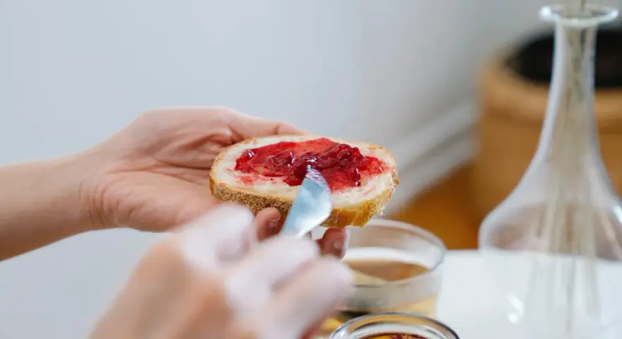 Hände verteilen Marmelade auf Brot. Ein süßer Genuss, der an die besonderen Gelüste in der Schwangerschaft erinnert.