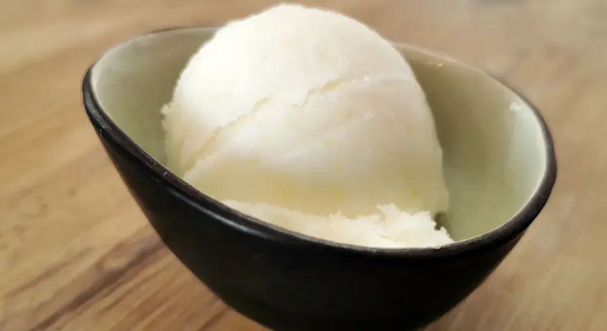 Ein Löffel cremiges Sorbet ohne Zucker in einer stilvollen Schale auf Holzhintergrund. Erfrischend und leicht.