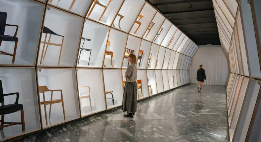 Wystawa krzeseł w muzeum designu Kopenhaga. Ludzie podziwiają ekspozycję w nowoczesnej, geometrycznej przestrzeni.