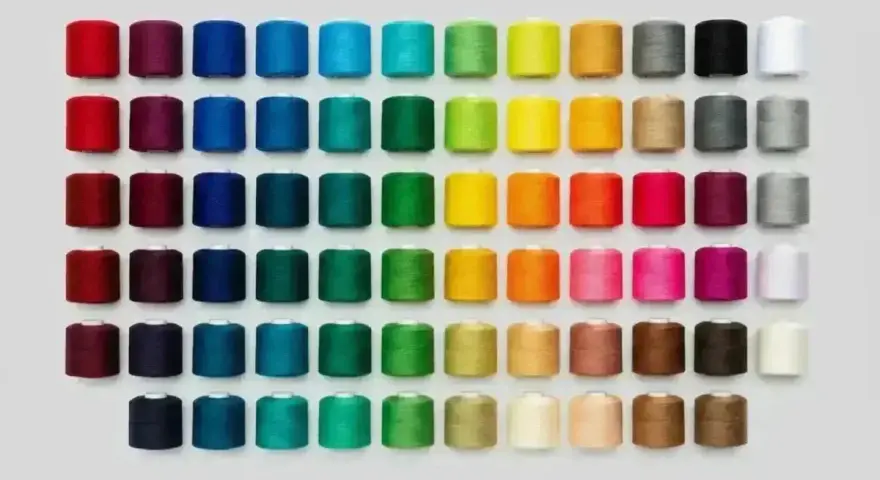 Una gran variedad de tipos de hilos de coser en carretes, organizados por color en filas y columnas.