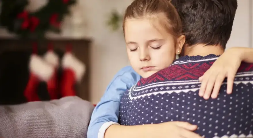 Dziewczynka mocno tuli tatę, który w świątecznej atmosferze, mimo że czasem dziecko terroryzuje rodziców, czuje się kochana.