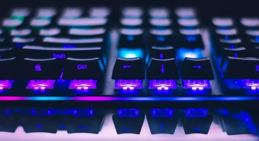 Zbliżenie na klawiaturę gamingową z kolorowym podświetleniem RGB. Widoczne klawisze Shift, Ctrl i strzałki. Różne rodzaje klawiatur oferują unikalne wrażenia.