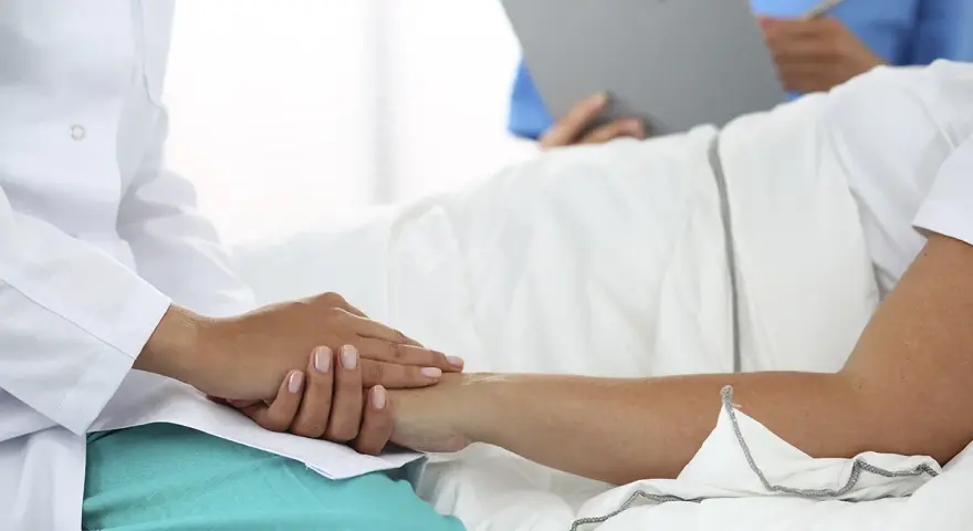 Lekarz w białym kitlu trzyma dłoń pacjenta, który leży w łóżku. To pokazuje, jaki lekarz nie może poślubić swojej pacjentki.