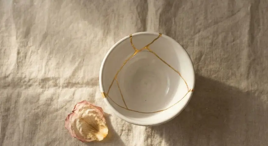 Biała miska z pęknięciami zespolonymi złotem, jak w kintsugi, obok zasuszonego płatka róży. Symbolizuje proces leczenia, jak w przypadku osobowości borderline test.