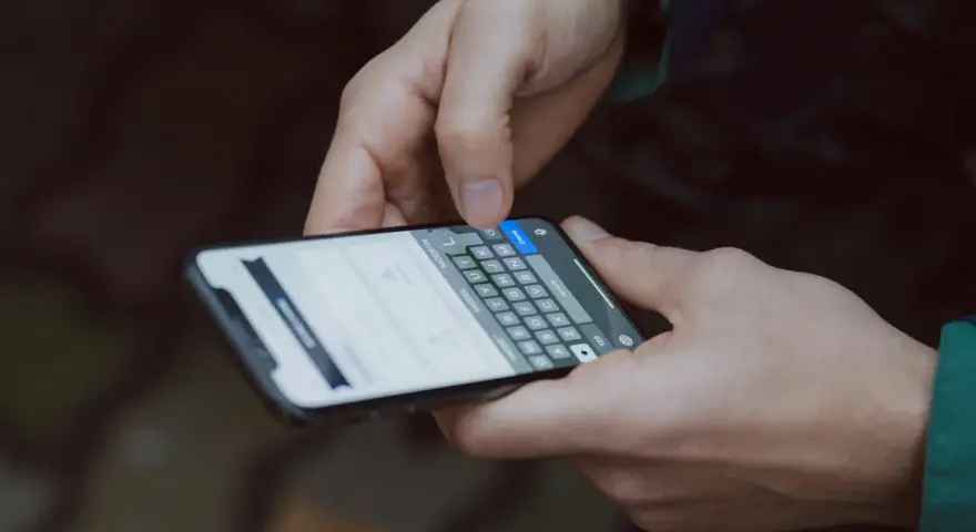 Dłonie trzymają smartfon z klawiaturą. Dowiedz się, jak wydrukować zdjęcie z telefonu, by zachować wspomnienia.