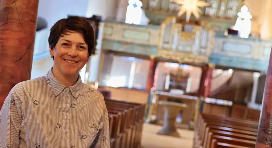 Eine lächelnde evangelische Pfarrerin steht in einer Kirche vor einer Orgel.