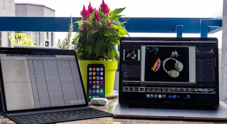 iPad Pro mit Tastatur, iPhone, AirPods und MacBook Pro mit Kopfhörern und Schlüsseln.