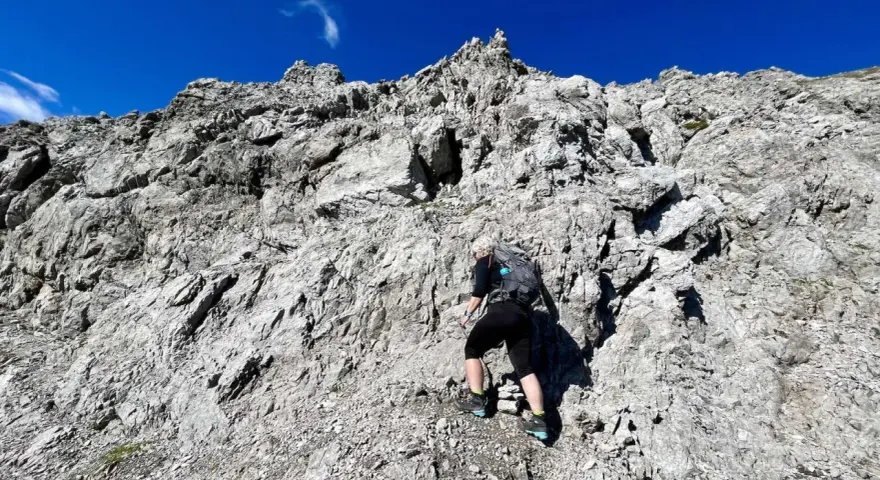 Bergsteigerin klettert über felsiges Gelände, das der UIAA-Skala entspricht. Blauer Himmel und schroffe Felsen.