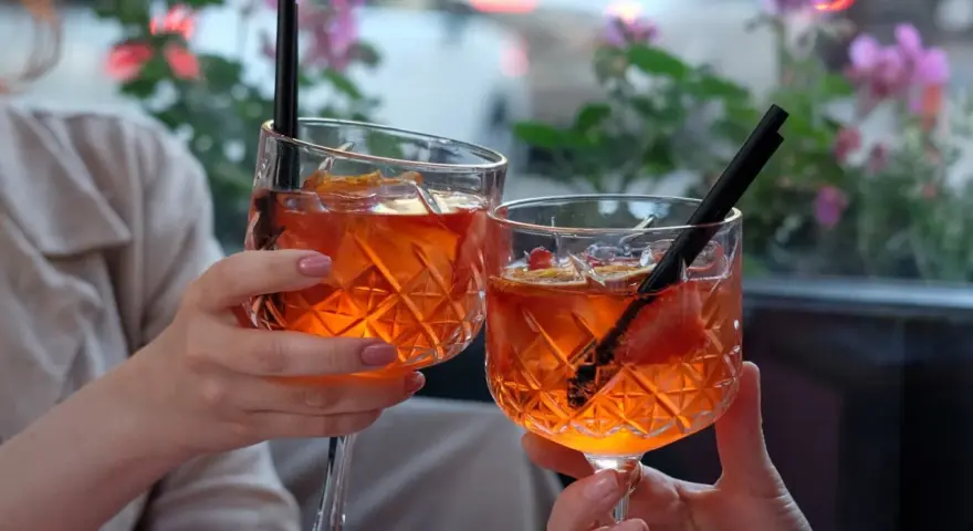 Dwie osoby wznoszą toast Aperolem. Orzeźwiający drink z pomarańczą i truskawką.