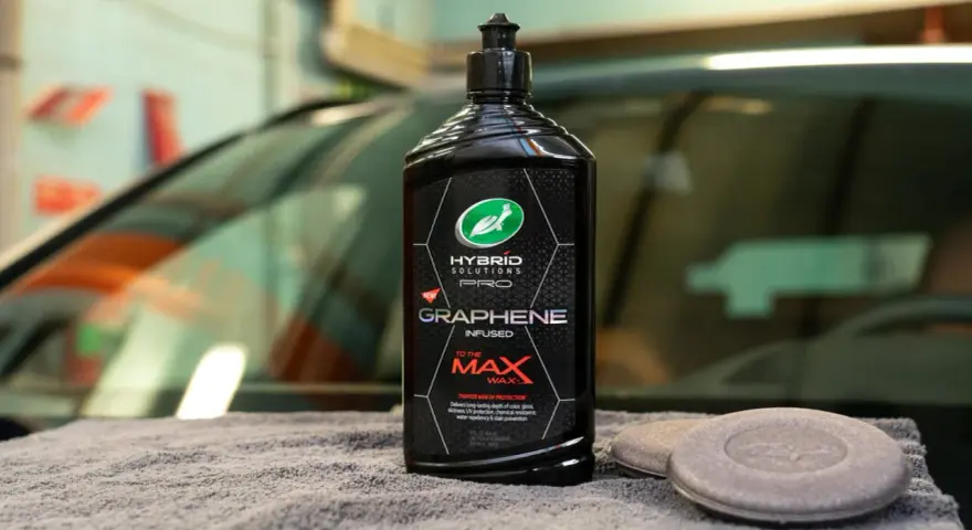 En flaska Turtle Wax Hybrid Solutions Pro Graphene Infused Wax, ett bilschampo för maximal glans och skydd, ligger på en grå handduk.