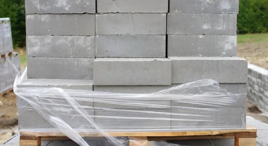 Stos betonowych bloczków fundamentowych na palecie, owiniętych folią.