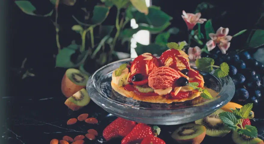 Eine süße Pizza mit Eis, Beeren und Kiwi. Mandeln und Trauben garnieren das Dessert.