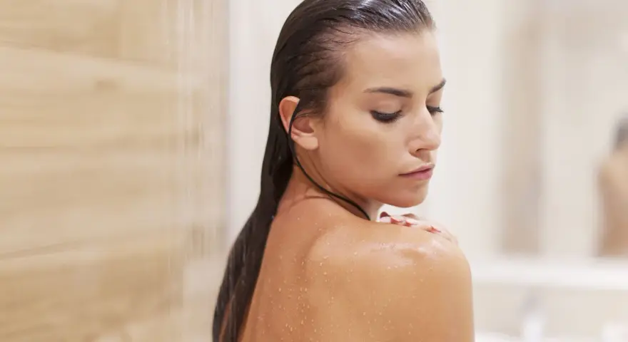 Mujer en la ducha, con gotas de agua en su piel. Pregúntate cada cuanto exfoliar el cuerpo para una piel radiante.
