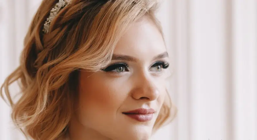 Eleganckie upięcia krótkich włosów na wesele z warkoczem i ozdobą. Delikatne fale i subtelny makijaż podkreślają urodę panny młodej.