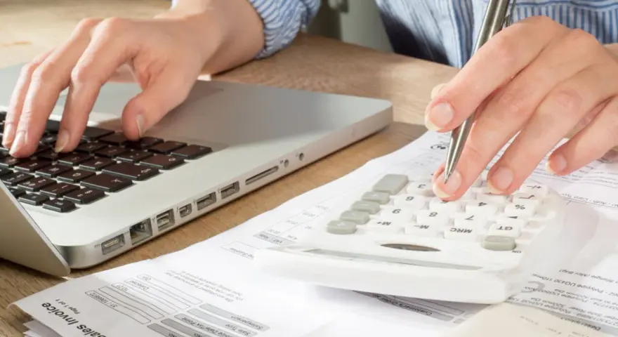 Main tenant calcule son solde de tout compte imposable sur une calculatrice, un ordinateur et des factures.