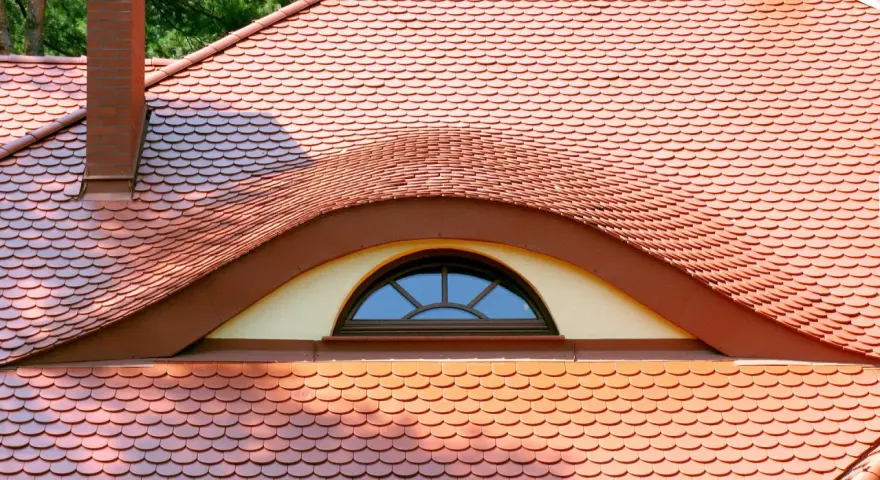 Ceglana dachówka ceramiczna w kształcie rybiej łuski, z ozdobnym lukarną. Idealna, by stworzyć stylowy dach.