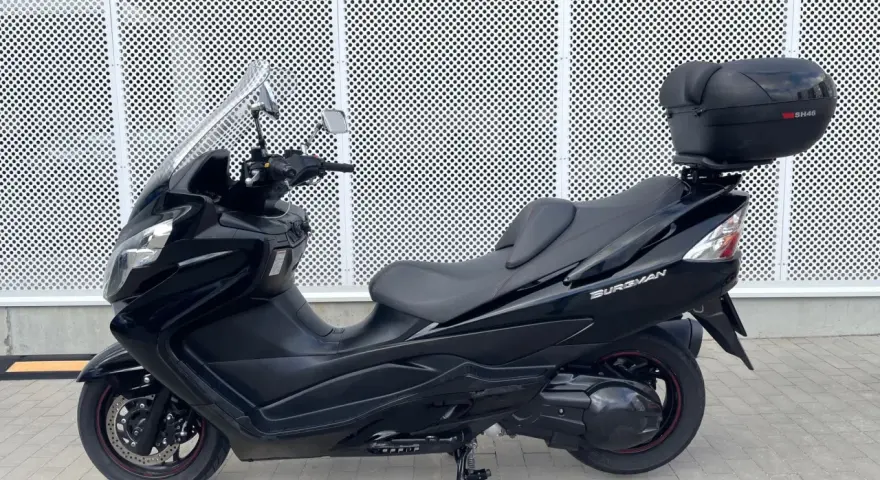 Czarny skuter Suzuki Burgman 400 z kufrem SH46 na tle perforowanej białej ściany.