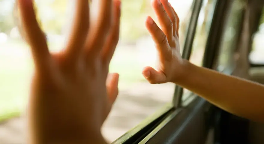 Dziecko z podwrażliwością dotykową delikatnie dotyka szyby samochodu, czując świat za nią.